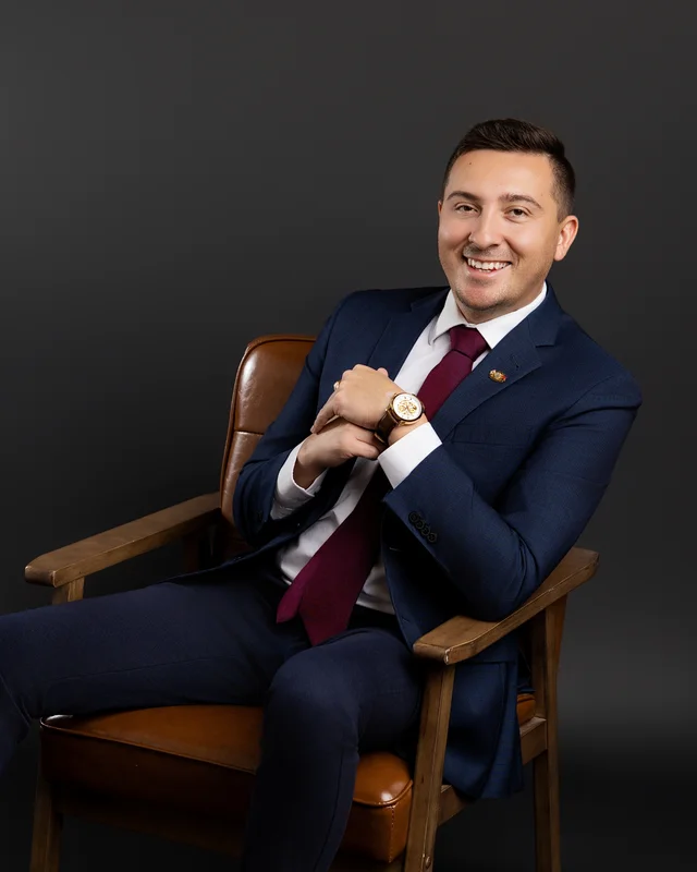John Maxwell seated in a chair, wearing a suit and tie.